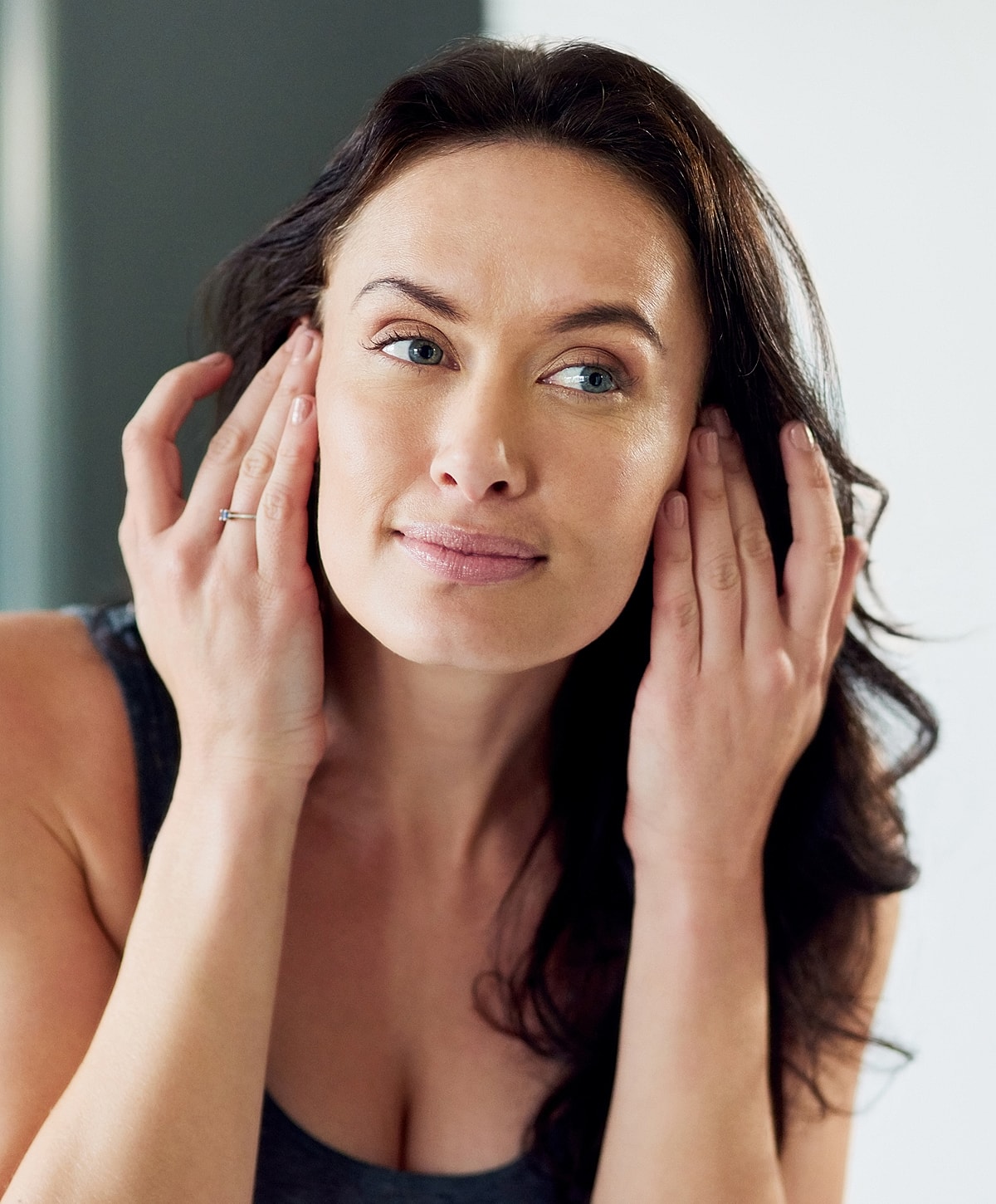 Woman touching face, looking thoughtful in mirror.