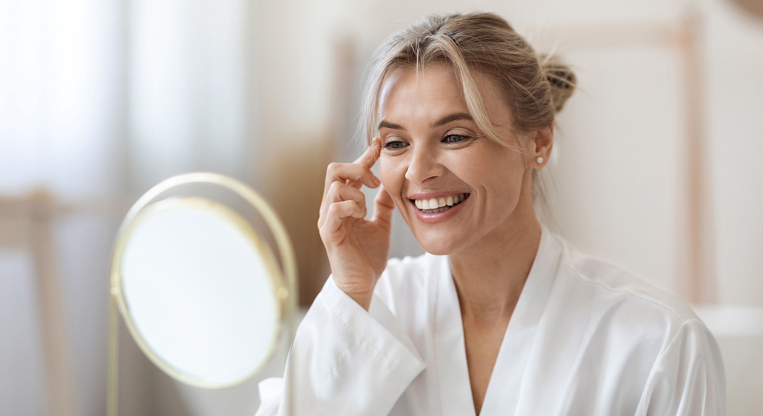 Woman applying skincare while smiling in mirror.